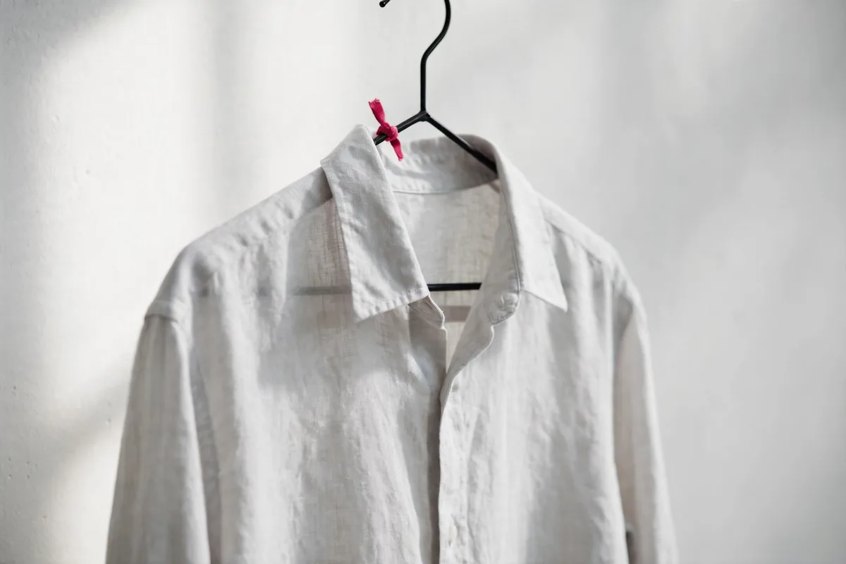A plain shirt on a hanger against a white wall