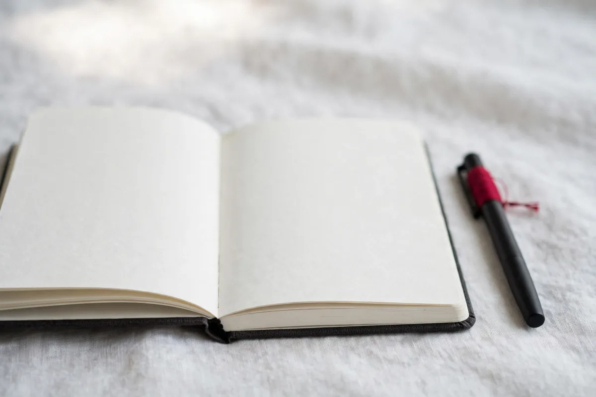 An open notebook with no writing beside a pen